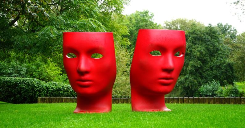 Act - Red Human Face Monument on Green Grass Field